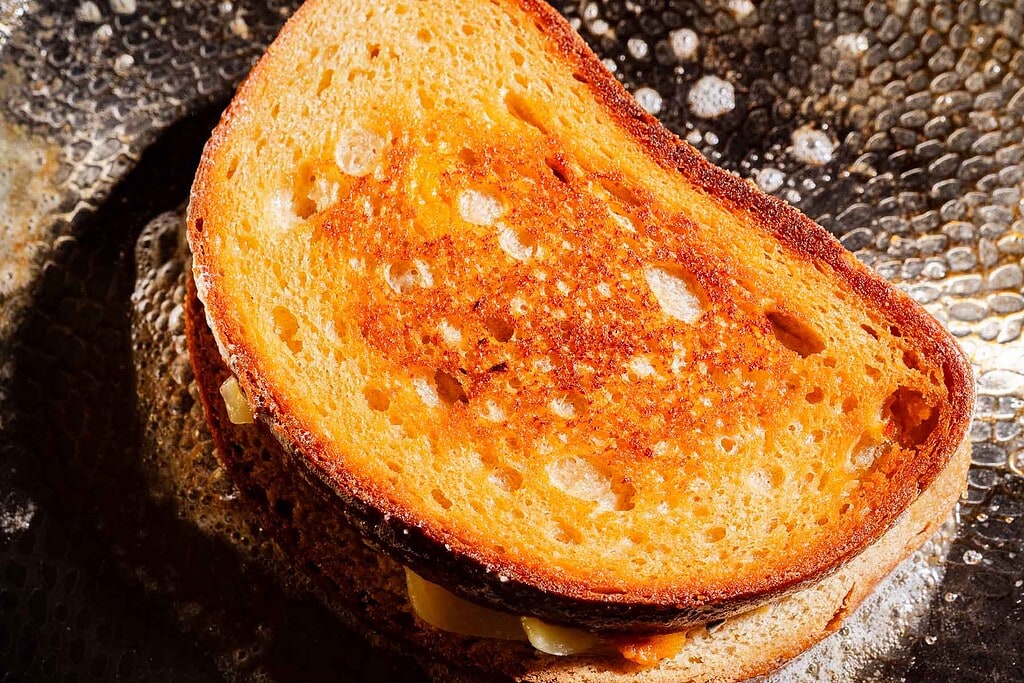 A close-up of a grilled cheese sandwich with golden brown, crispy bread and melted cheese, sitting in a pan with bubbling butter.