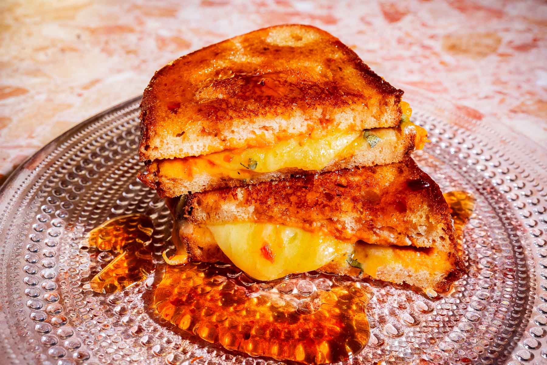 Pumpkin grilled cheese sandwich cut in half and stacked on a clear plate, with melted cheese and chili oil dripping onto the plate.