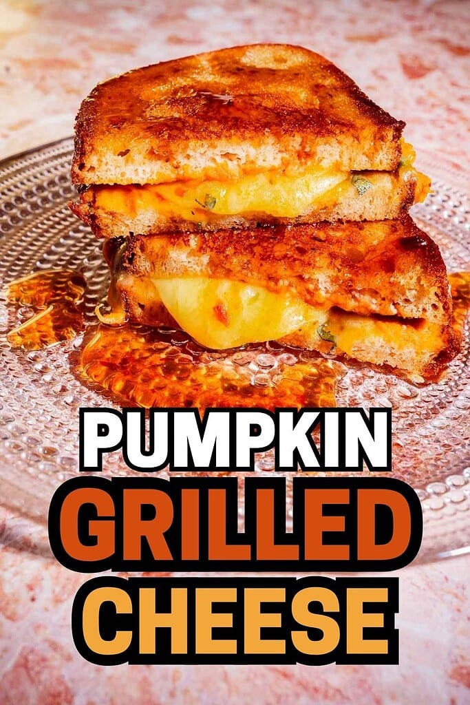 A stack of pumpkin grilled cheese sandwiches with melted cheese on a glass plate. Text overlay reads “Pumpkin Grilled Cheese.”.