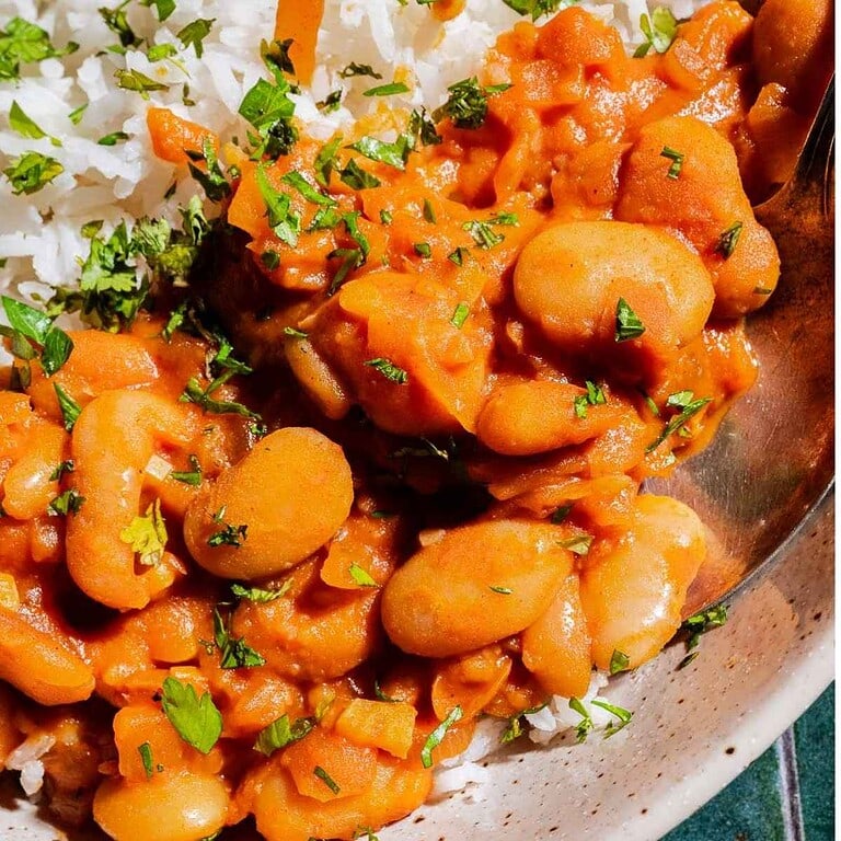 Close-up of a plate with white rice and creamy tomato-based beans, garnished with chopped fresh herbs.