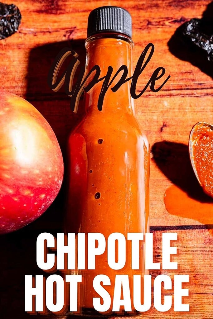 A bottle of apple hot sauce sits on a wooden surface next to an apple and a spoon with sauce. The text reads “Apple Chipotle Hot Sauce.”.