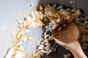 Diced onions being sautéed in a pan with a wooden spoon, lightly coated with oil, form the savory base for a hearty chickpea soup.