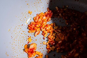 Chopped onions and tomato paste sautéing in a pan for a hearty chickpea soup, with a portion of the pan in shadow.