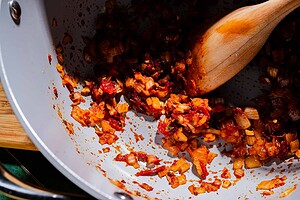 Diced onions and tomatoes sautéing in a pan with a wooden spoon, showing caramelization and rich color, as the base for a flavorful chickpea soup.