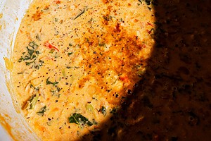 Close-up of a creamy, orange-colored chickpea soup with visible herbs and spices, partially shaded on one side.