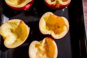 Hollowed-out apple halves sit on a black baking tray, their empty centers ready to be transformed into a delightful apple creme brulee, prepared for filling or baking.
