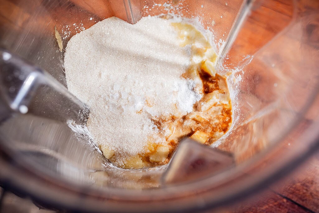 Sugar, vanilla extract, and other baking ingredients in a blender viewed from above, ready to be mixed for a delicious apple creme brulee creation.