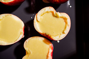 Halved apples with centers filled with a pale yellow apple creme brulee custard, placed on a dark baking sheet.