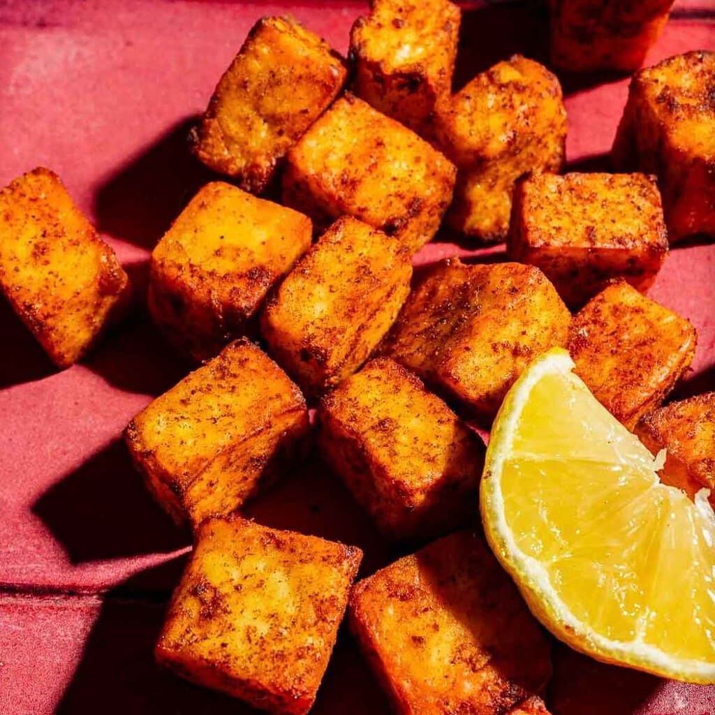 Crispy seasoned tofu cubes served with a lemon wedge.