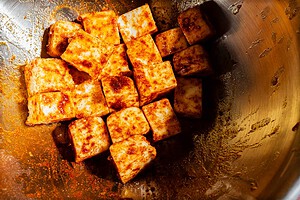 Cubed tofu coated in a reddish-brown spice blend inside a metal mixing bowl.
