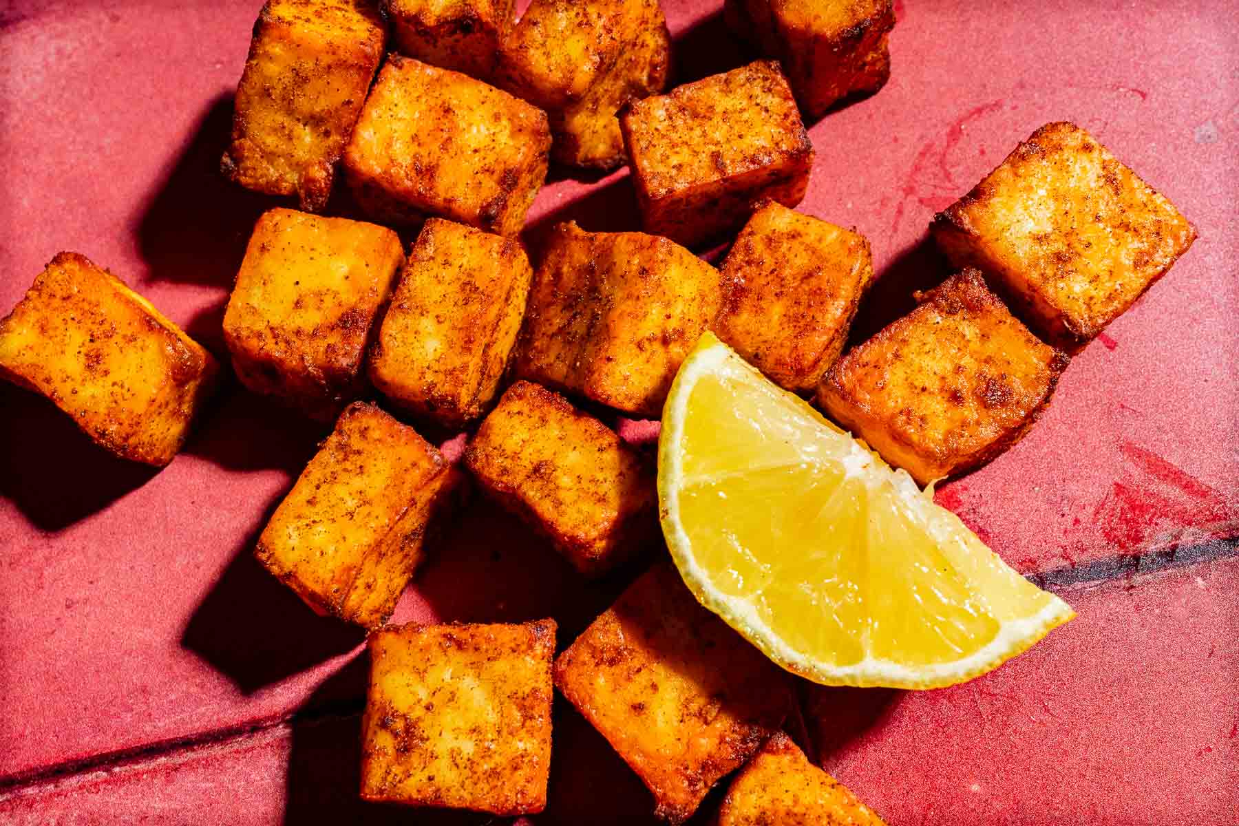 Crispy seasoned air fryer paneer cubes served with a fresh lemon wedge on a red surface.