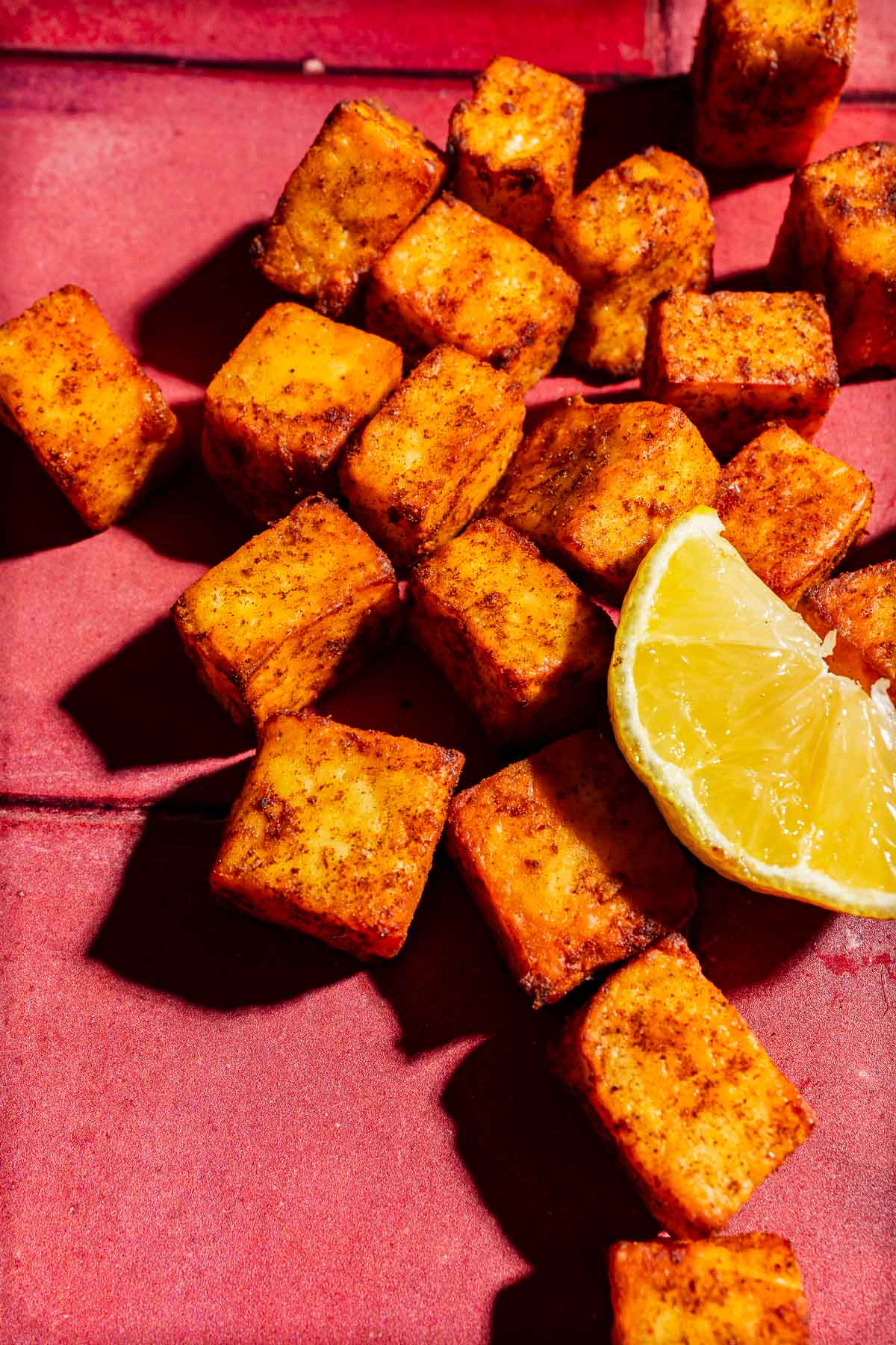Seasoned, golden-brown air fryer paneer cubes with a lemon wedge on a red surface.