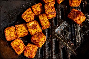 Seasoned, cubed tofu cooking in an air fryer basket.