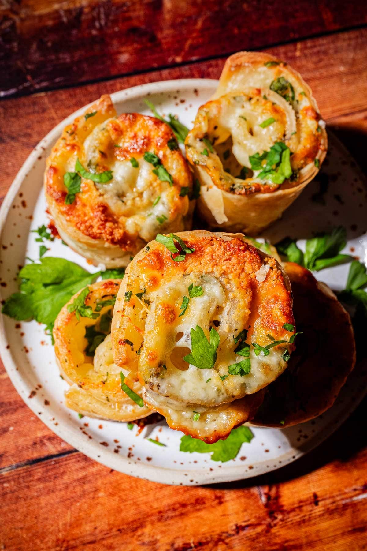 Savory baked pastry rolls topped with melted cheese and fresh herbs on a speckled plate.
