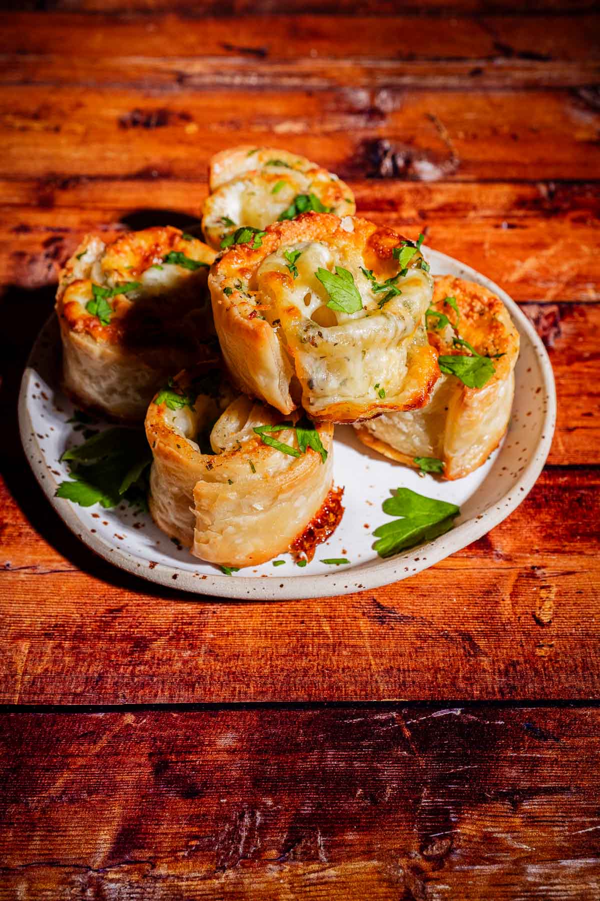 A plate of five golden-brown, spiral-shaped savory pastries topped with fresh green herbs.