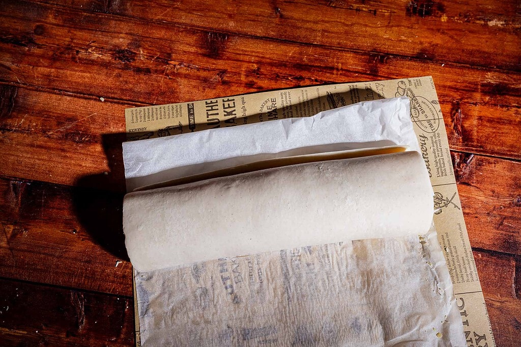 A roll of unbaked puff pastry on branded parchment paper atop a wooden table.