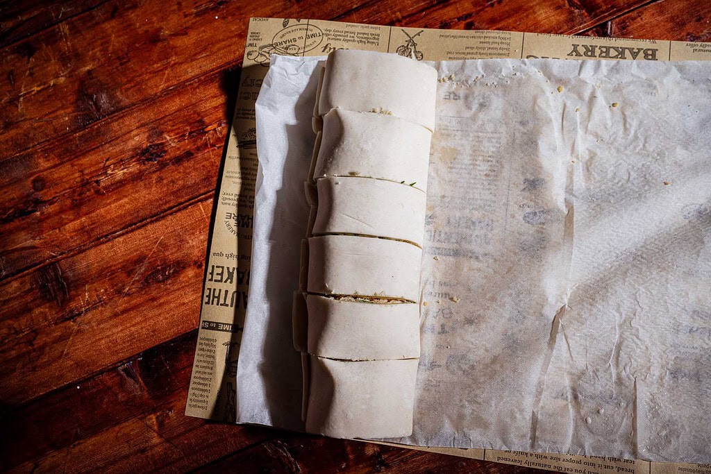 Sliced puff pastry rolls sitting on parchment paper printed with bakery text.