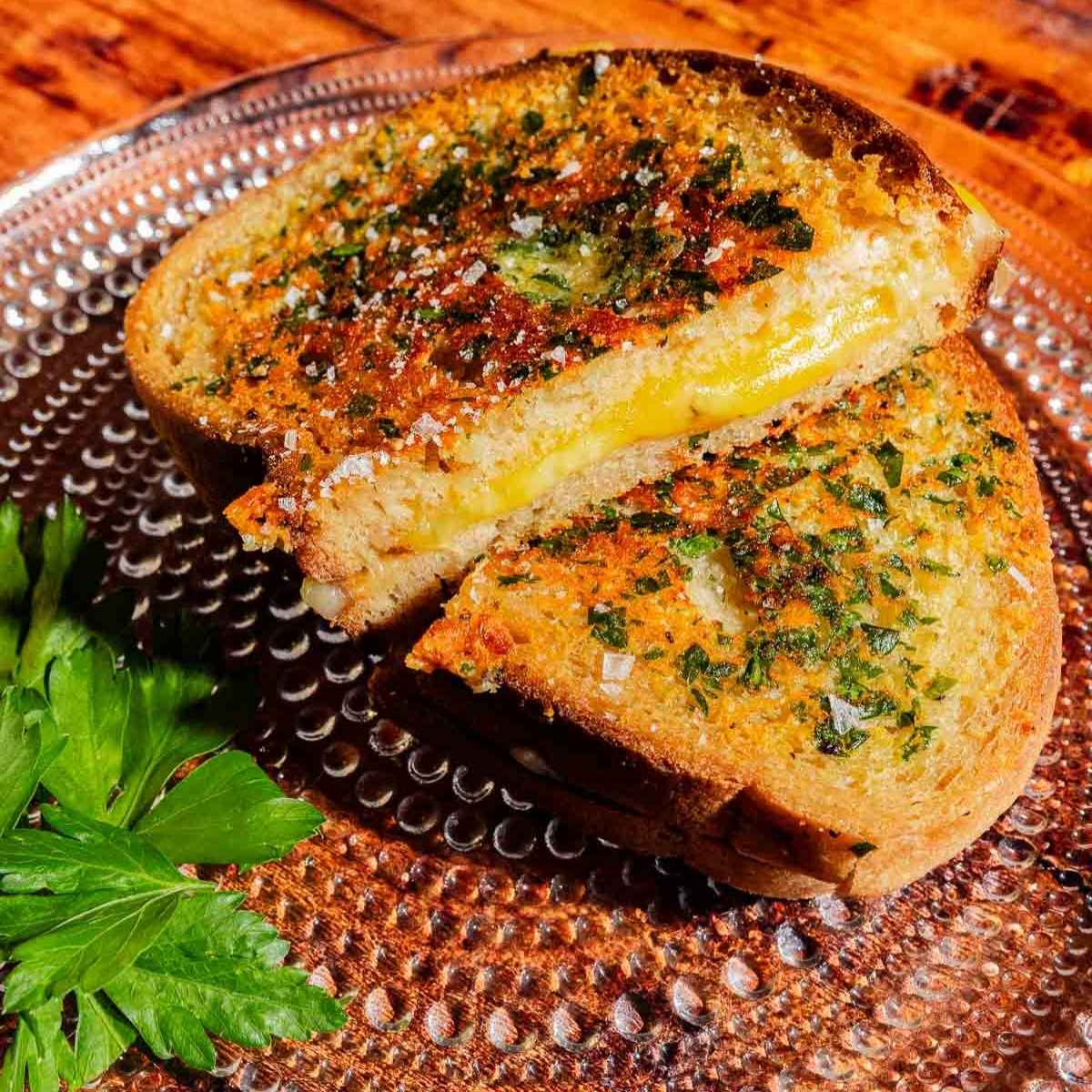A grilled cheese sandwich on toasted, herb-crusted bread, cut in half on a textured glass plate.