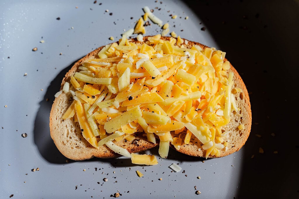 A slice of cheesy garlic bread topped with cracked black pepper.