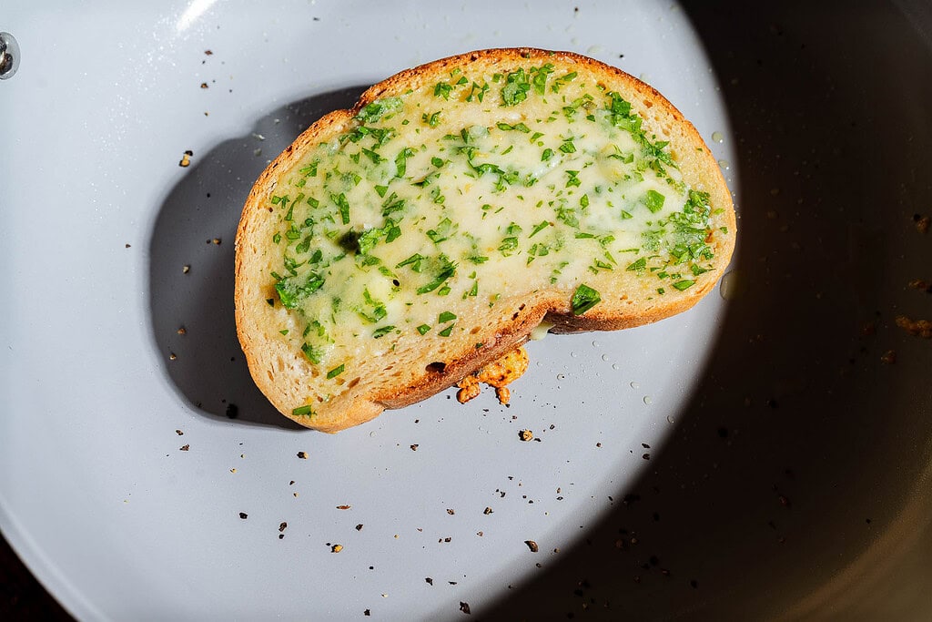 A single slice of garlic bread grilled cheese topped with fresh herbs in a frying pan.