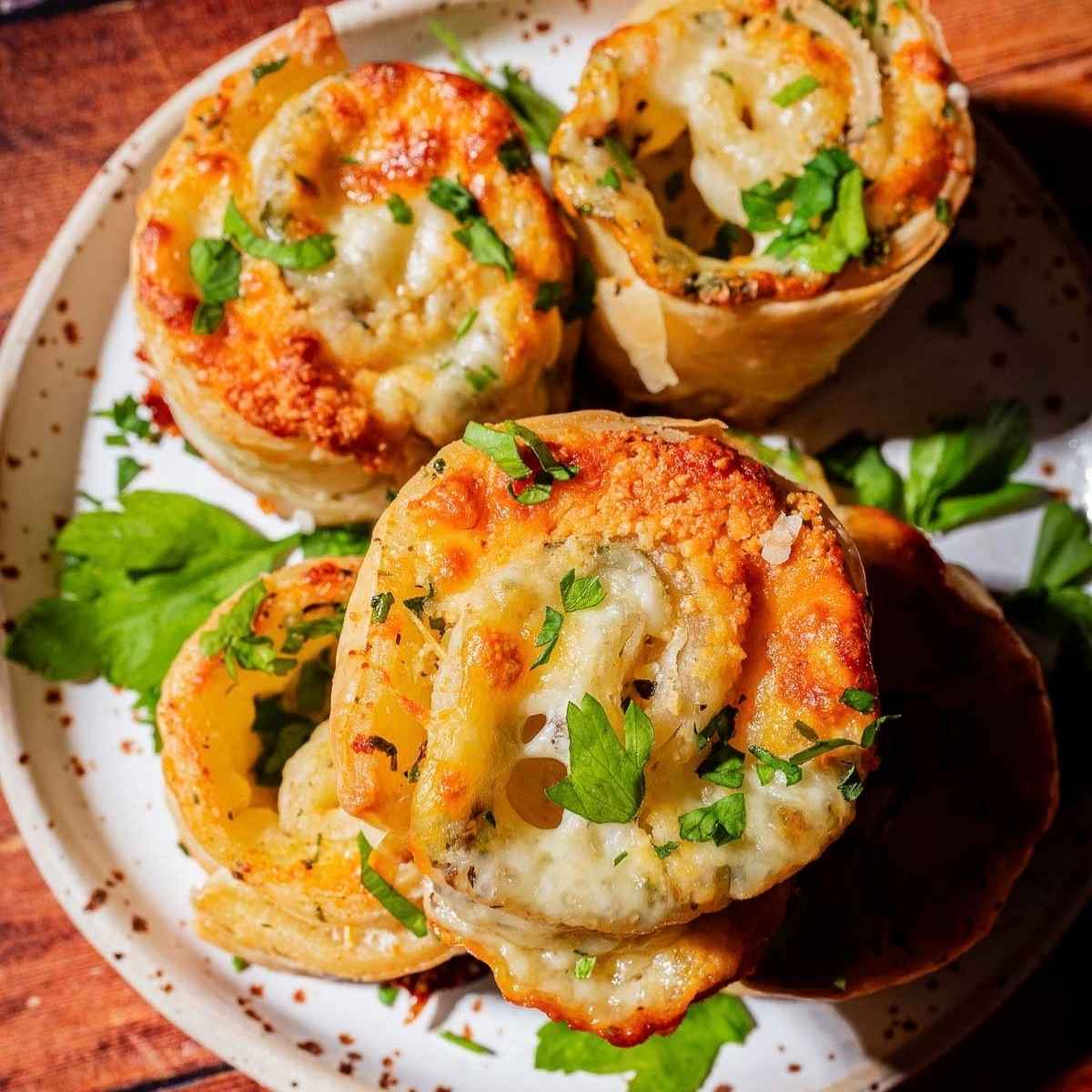 Four baked, spiral-shaped appetizers topped with melted cheese and fresh herbs on a speckled plate.