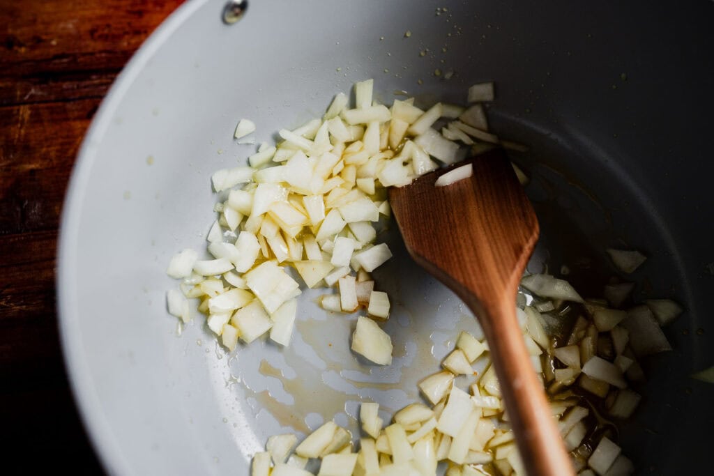 Diced onions for a marry me chili saut&eacute;ing in a grey pan with a wooden spatula.