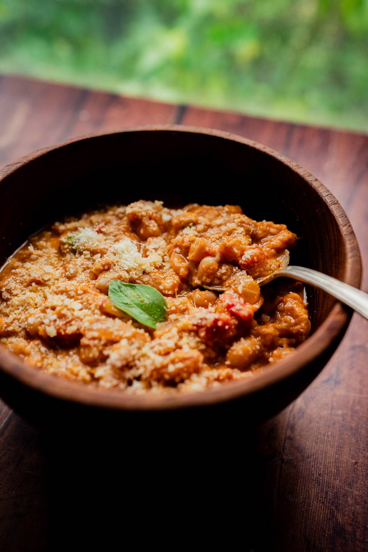 A wooden bowl of marry me chili topped with parmesan and a basil leaf, with a spoon resting inside.