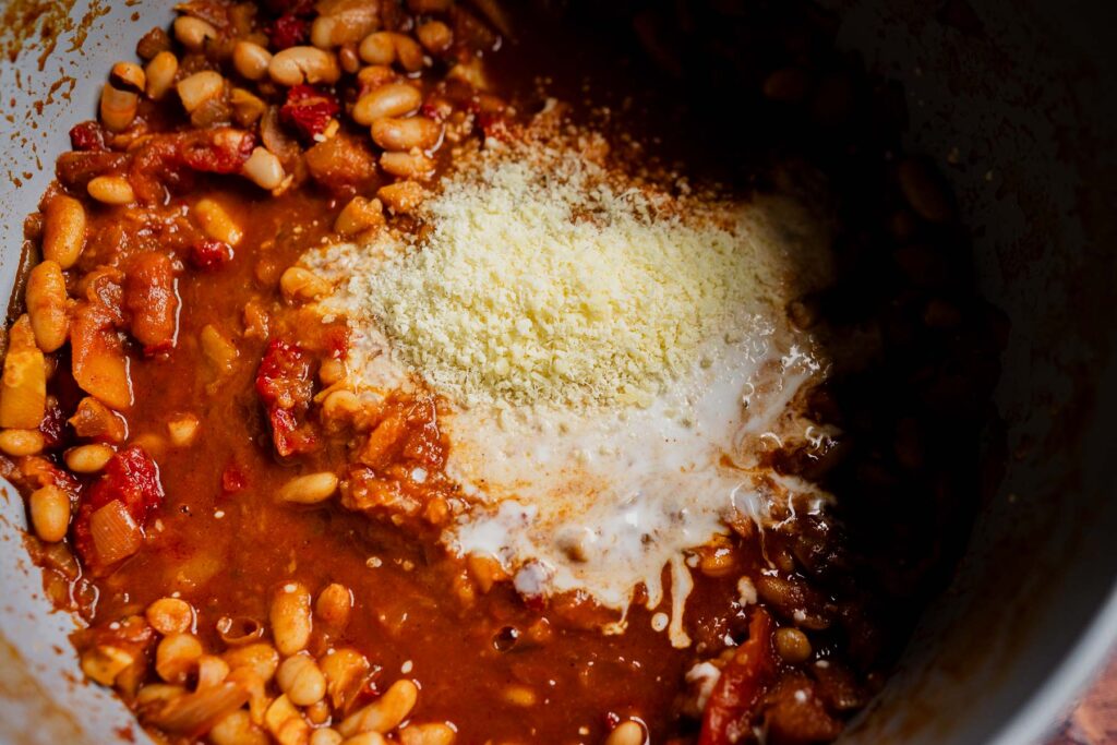 A pot of marry me chili topped with a mound of grated cheese and a swirl of cream.