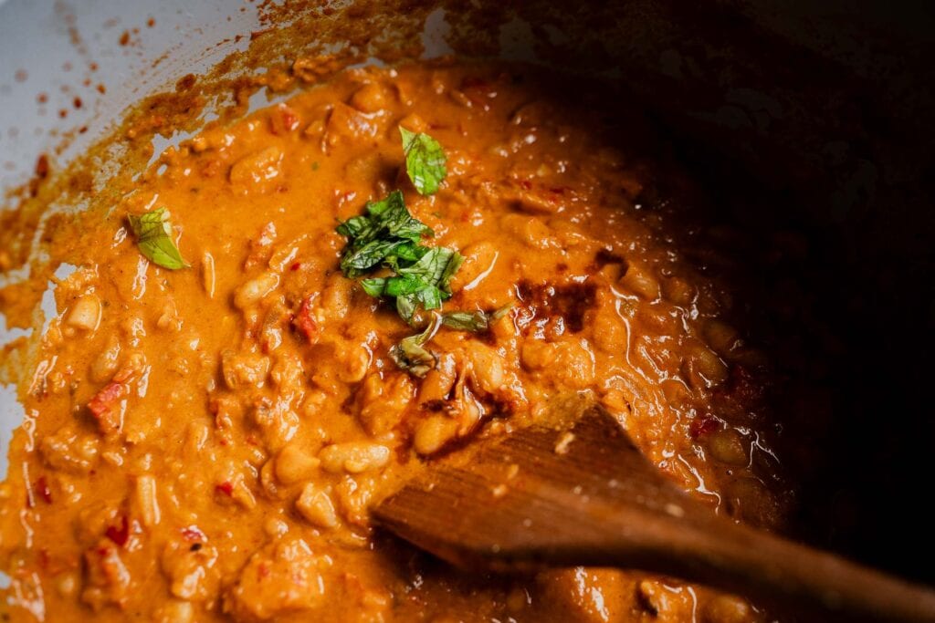 Creamy tomato-based marry me chili in a pot, garnished with fresh herbs and stirred with a wooden spoon.