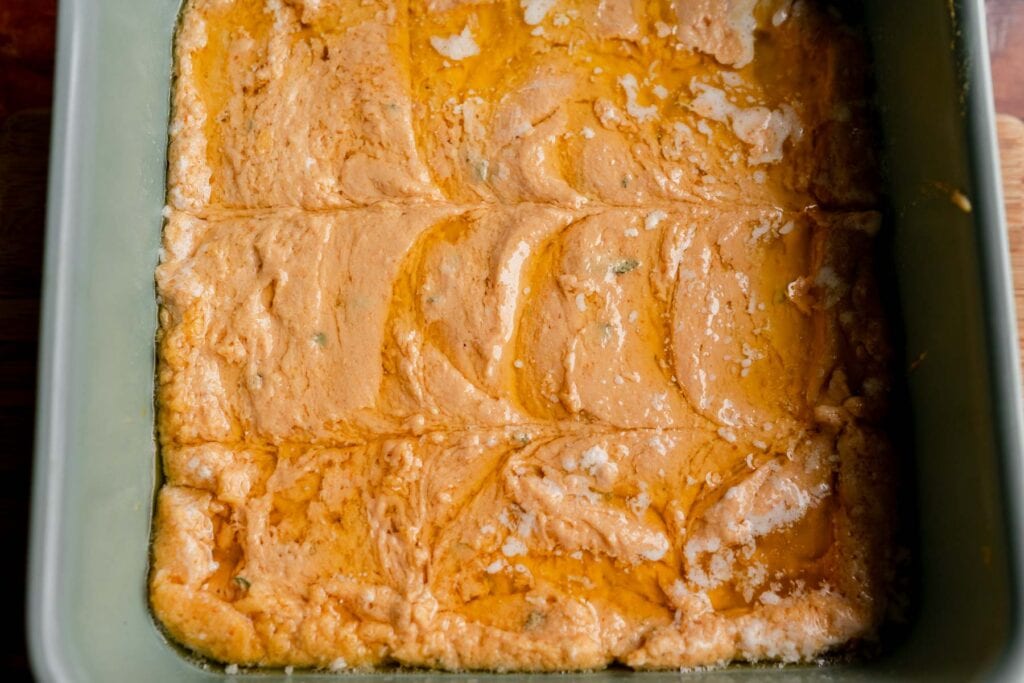 A square baking dish containing baked pumpkin butter swim biscuits with an orange hue and visible pools of oil on the surface.