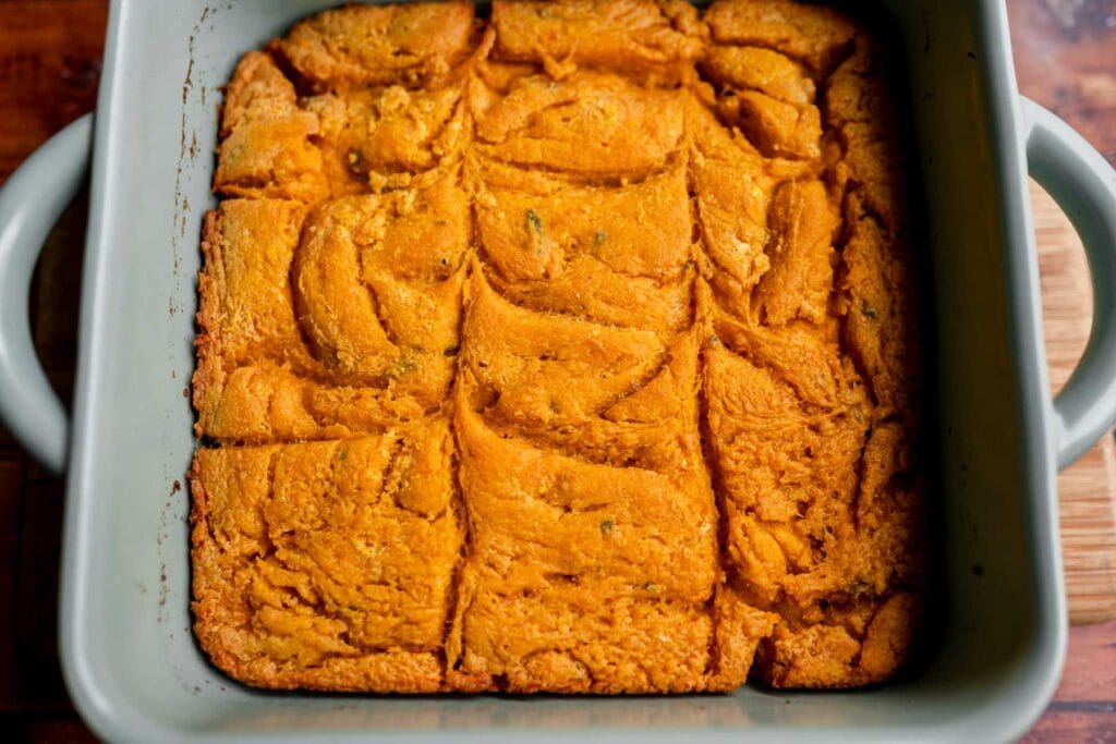 A square baking dish containing freshly baked, golden-brown pumpkin butter swim biscuits cut into large square pieces.